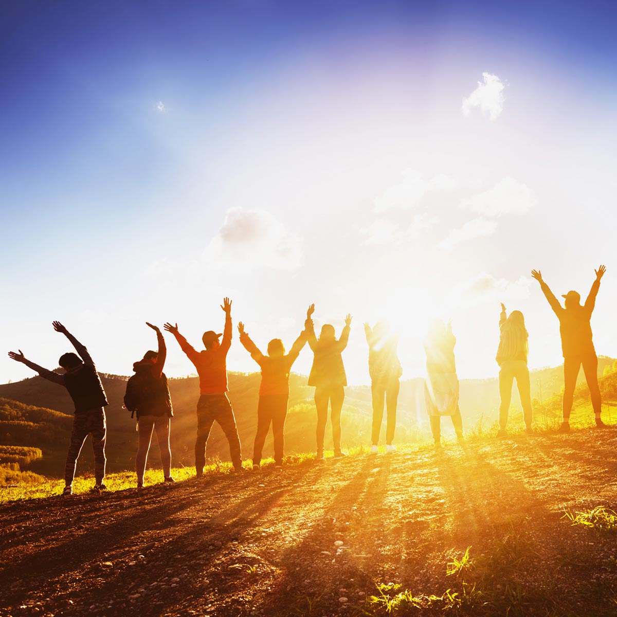 line of people on hill at sunset raising their hands in unison