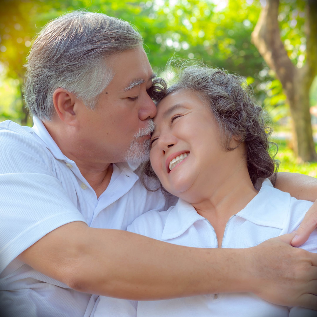 husband kissing wife on forehead in backyard