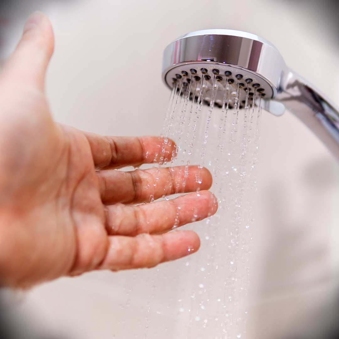 person holding hand under shower head to check temperature of water