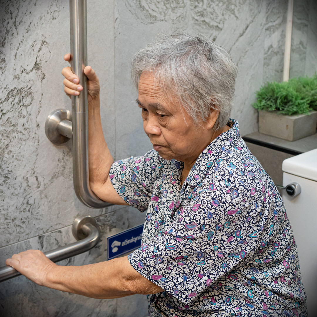 woman using safety bar to pull herself up off of toilet