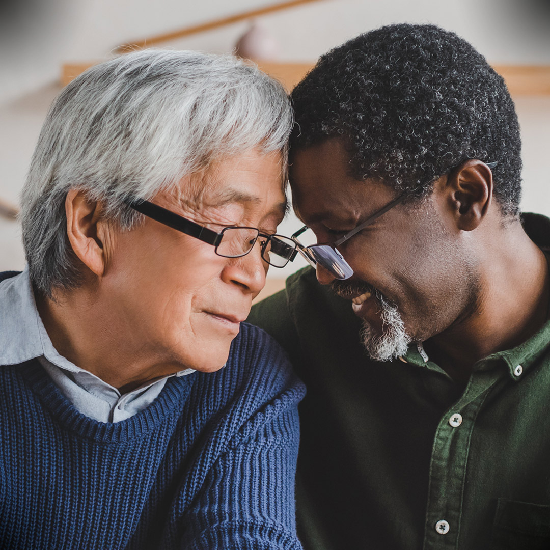 two older men at dining table with heads together and embracing