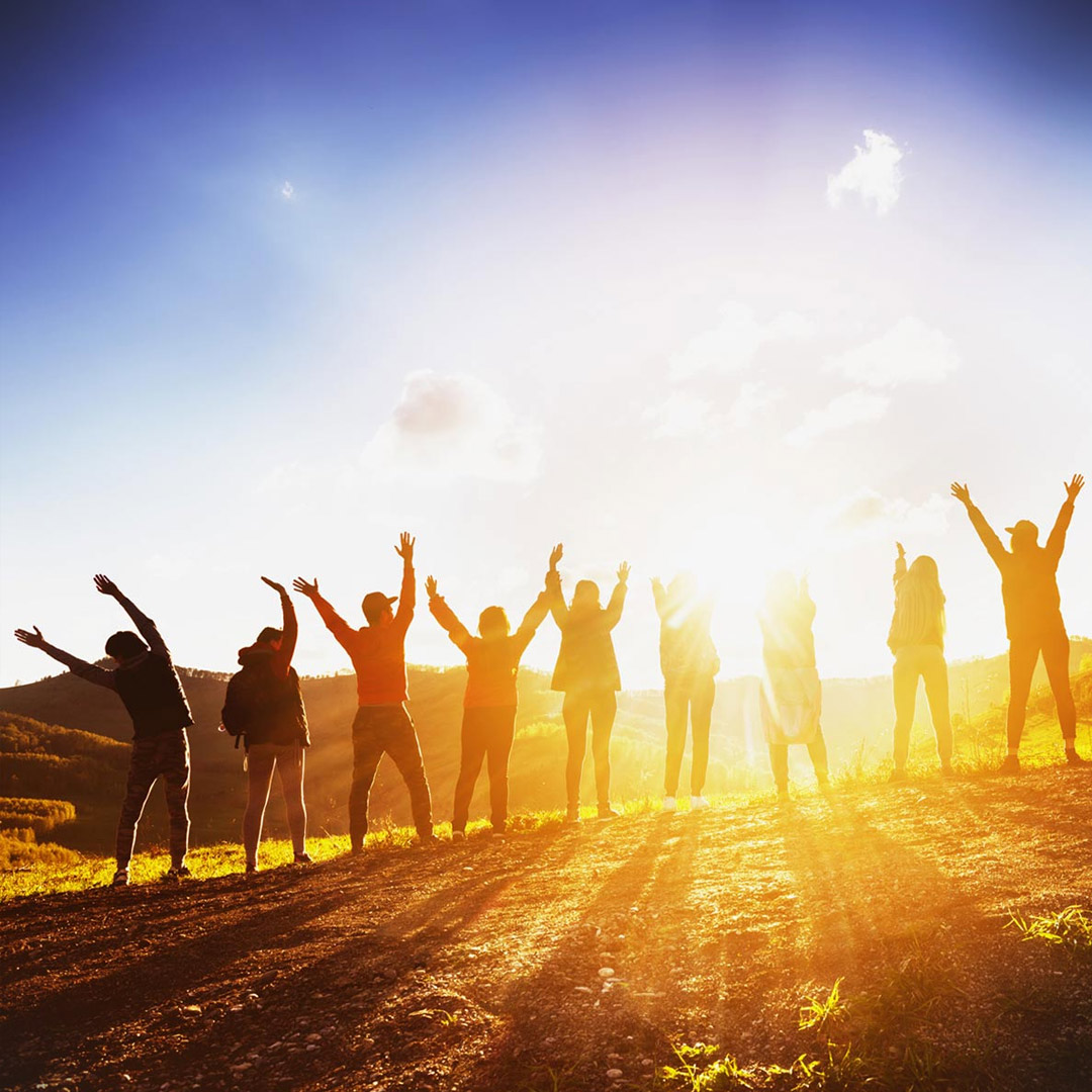 people on a hill at sunset raising hands together