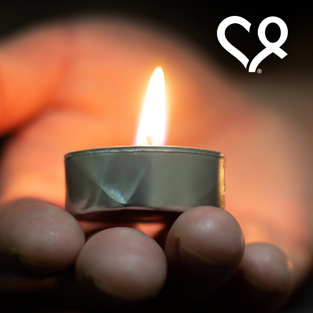 tribute-donations hand holding burning votive candle
