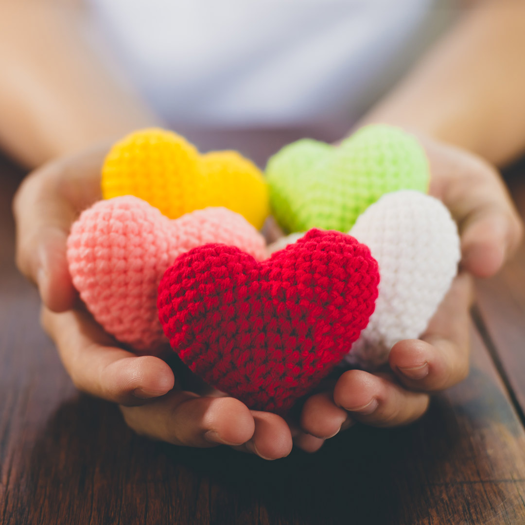 hands holding knitted hearts in different yarn colors