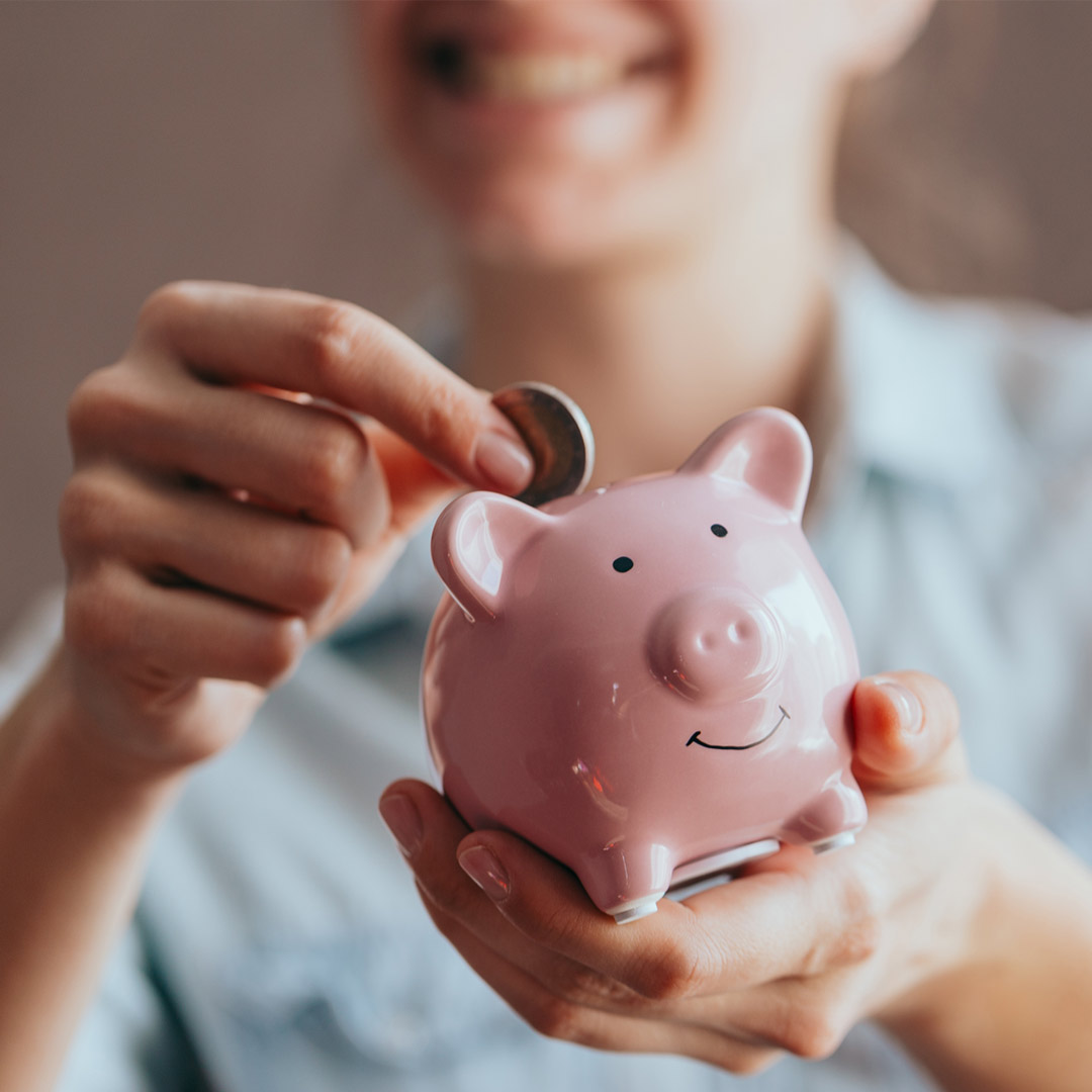 woman smiling and putting coin in piggy bank