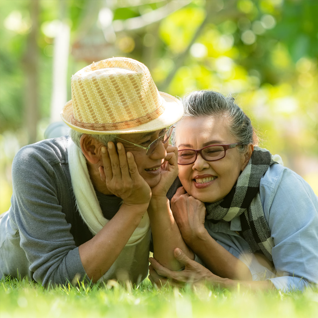 man and woman smiling and lying in the grass propped up on their elbows