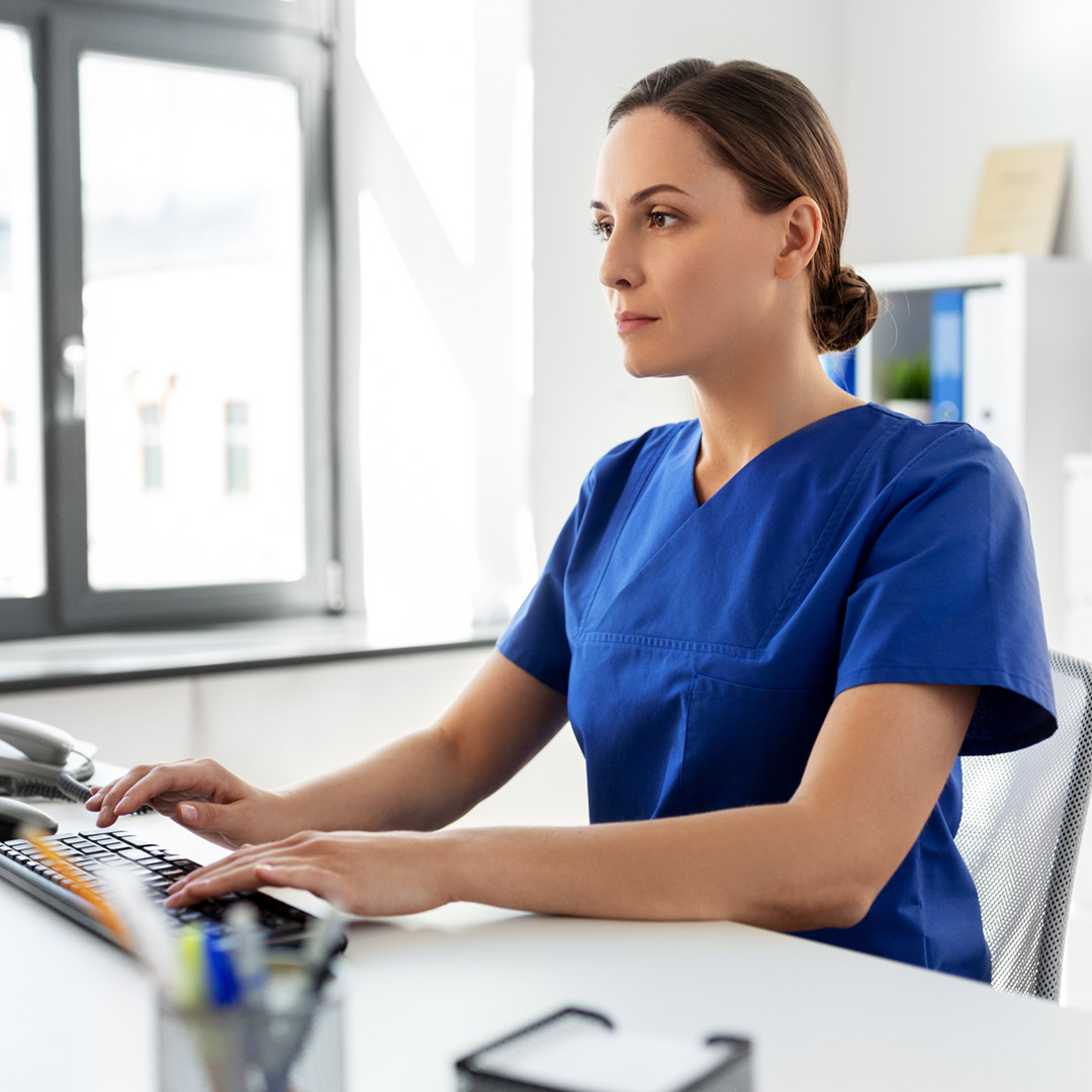 woman in scrubs sitting at computer
