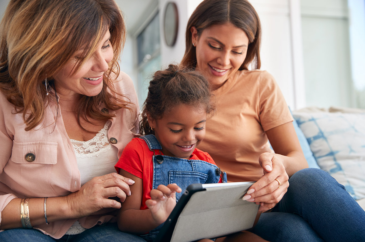 grandmother, mother and granddaughter on couch reading tablet together