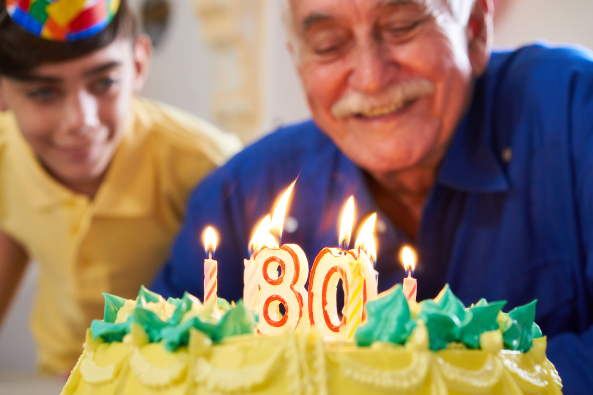 80 year old man blowing out candles on his birthday cake with grandson