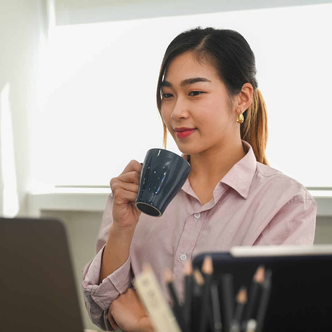 woman holding coffee cup and looking at her laptop screen