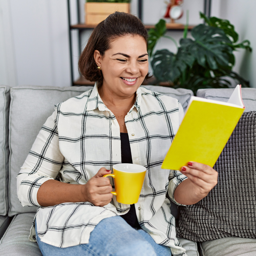 woman sitting on couch having coffee and reading a book