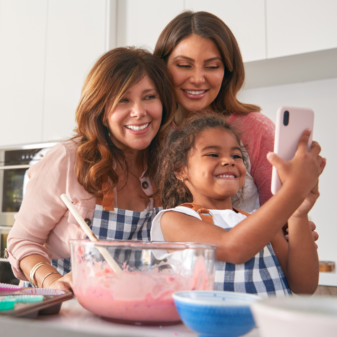 Grandmother, mother, and granddaughter taking selfie in kitchen