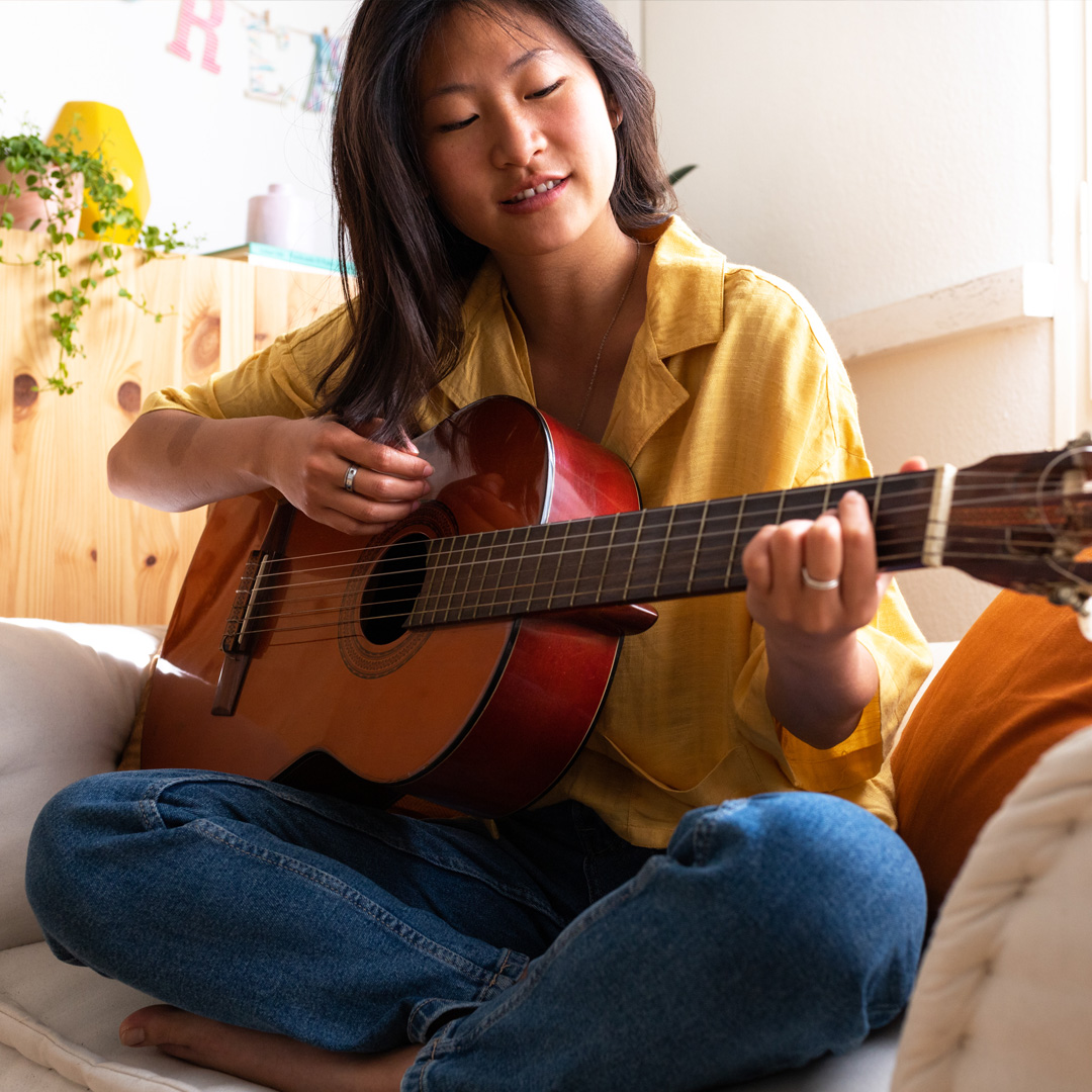 woman sitting on couch playing acoustic guitar
