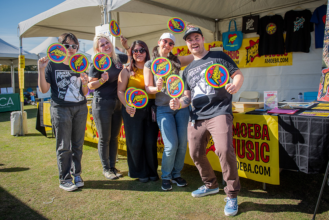 People posing with branded fans at the Amoeba Music booth