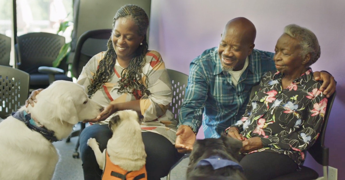 A family petting dogs and smiling at a Memory Mornings event.