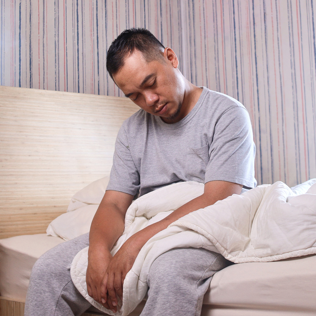 man sitting on edge of bed still asleep