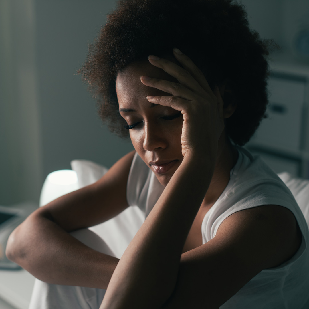 woman sitting up in bed and putting her hand to her head